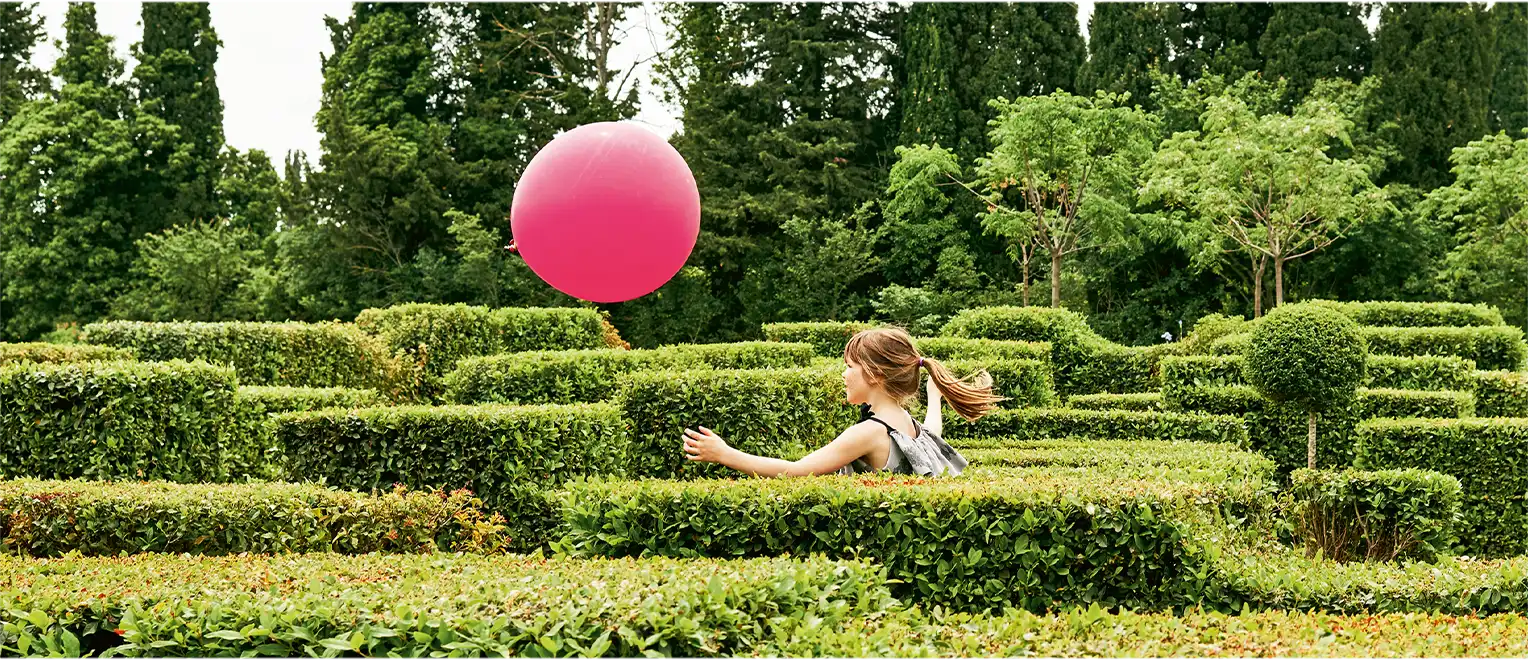 A little girl runs after a magenta balloon in a maze. (photo)