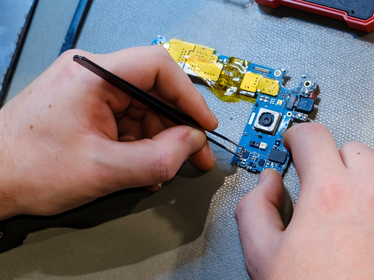 Somebody is working on a microchip or board that has been disassembled, with one component being placed into its original location inside another housing.