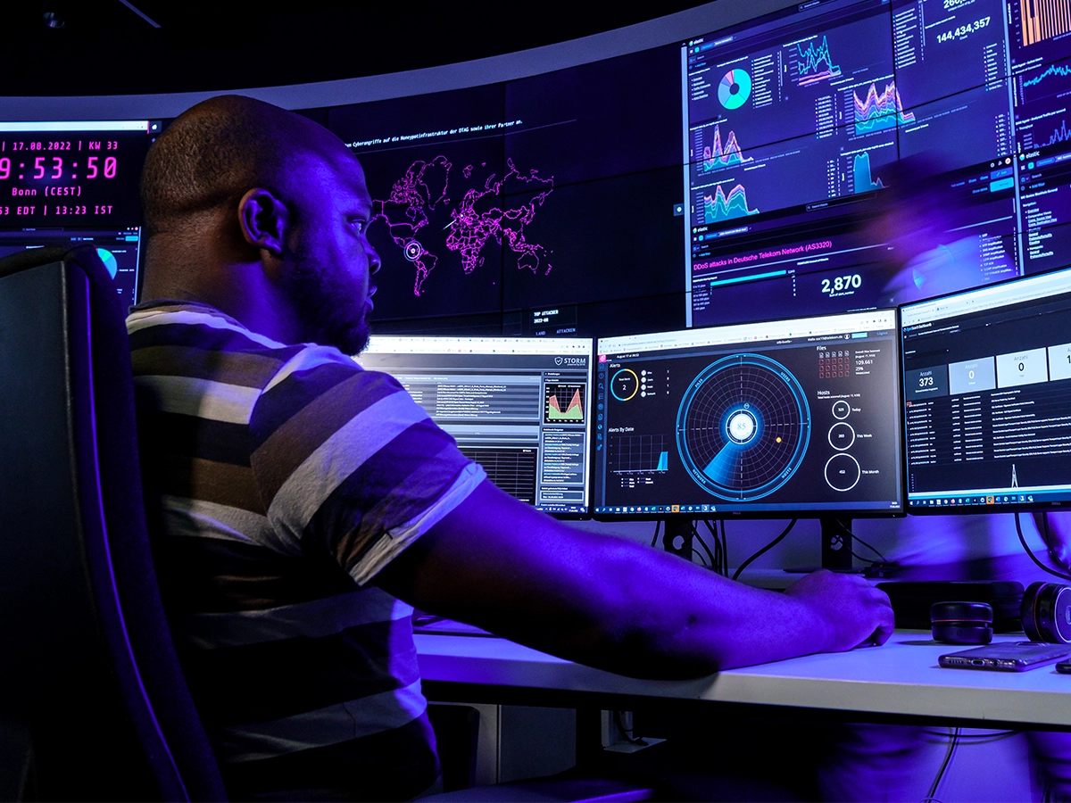 This image shows a person sitting at a computer with multiple screens displaying various data and analytics.