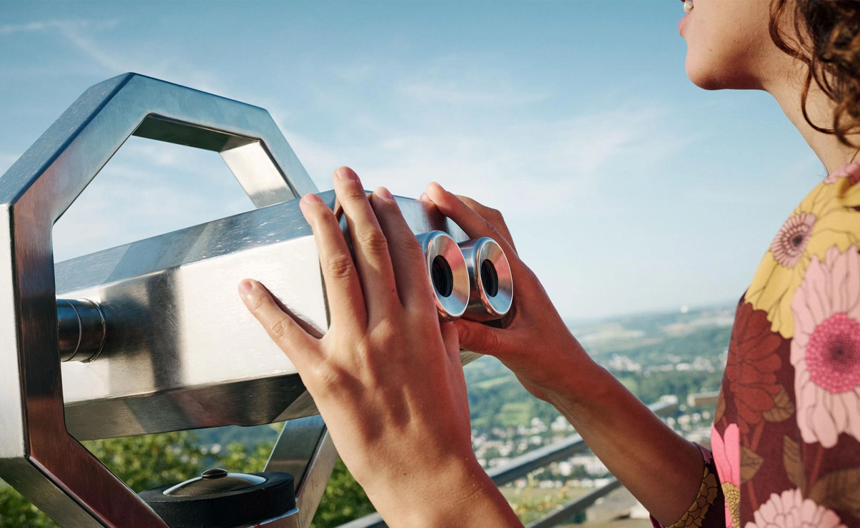 This image shows a woman holding binoculars typically used on towers or high points for sightseeing.