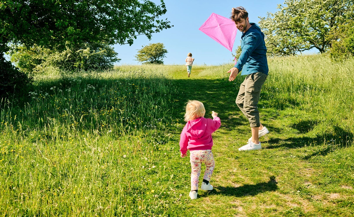 In the image, there are two individuals, an adult and a child. The adult is holding a colorful kite and appears to be preparing to fly it, given the position of the kite and the open space behind them. The people are outside.