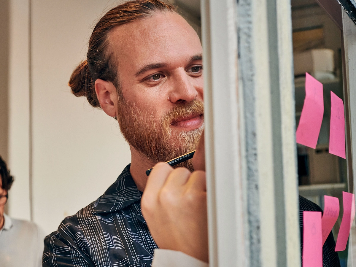 The image shows a man writing on paper which sticks to a glass board.