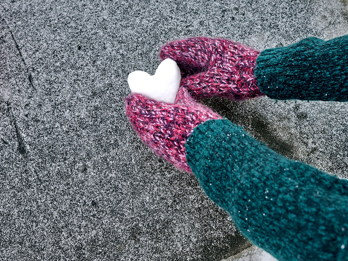 A person places a snow heart on the ground. The person is wearing gloves and a sweater.