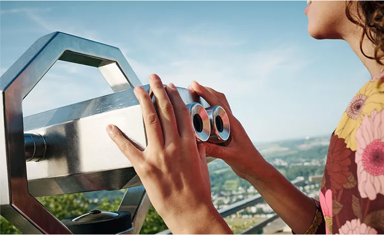 Woman holding binoculars which point to a green landscape. (Photo)