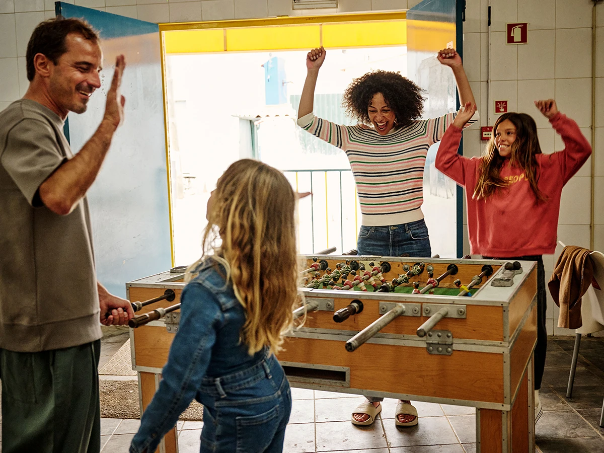 A man, woman, and two girls are celebrating around a foosballtable (Header Photo)